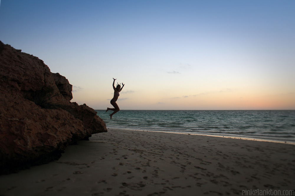 person jumping from cliff on beach