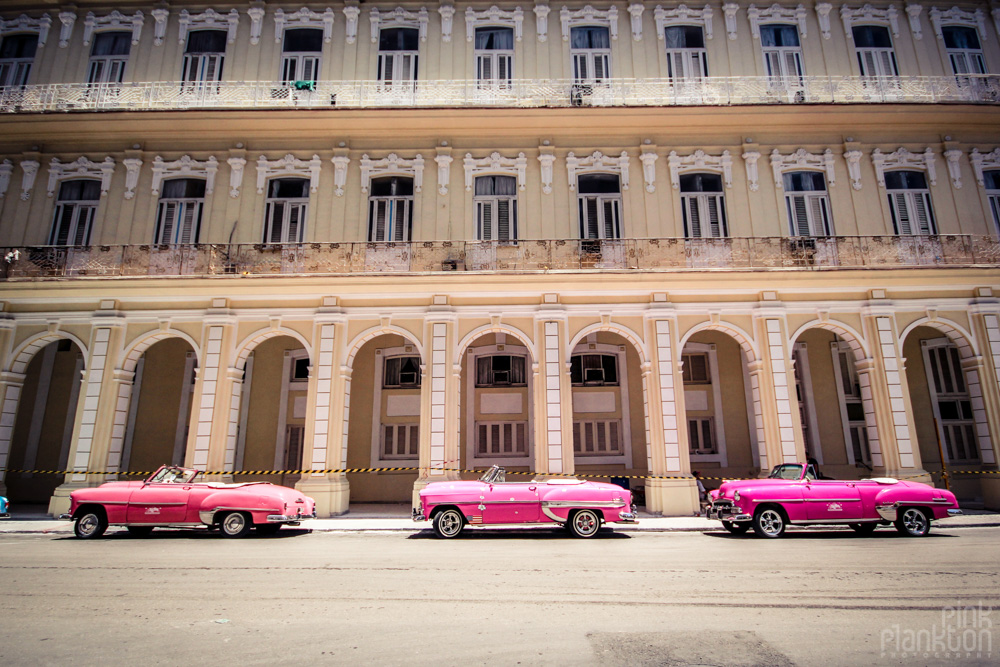 3 pink classic cars in Havana Cuba in front of colonial architectural building