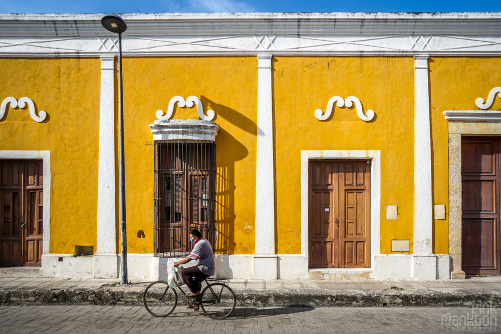 man riding bike past yellow buildings in Izamal, Mexico