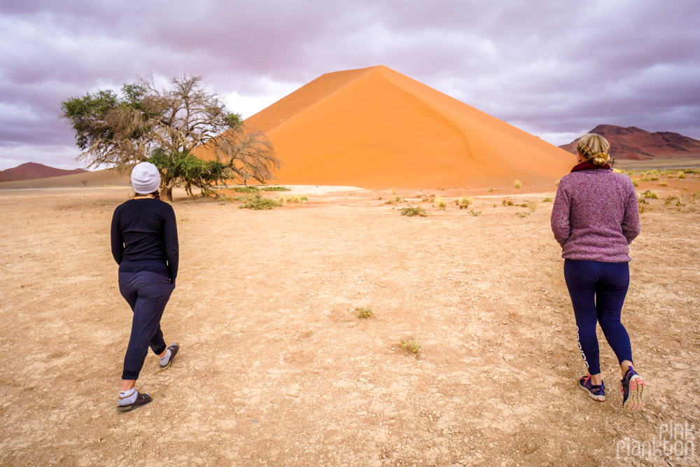 Two women walking towards giant sand dune in Sossusvlei, Namibia