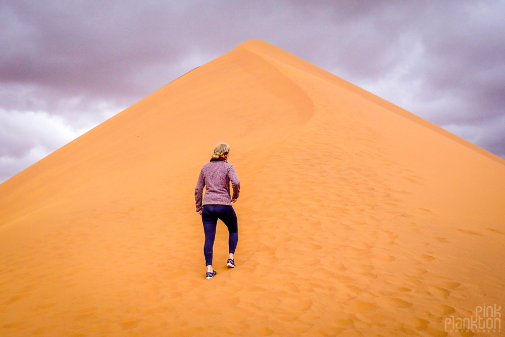 Woman walking up giant sand dune in Sossusvlei, Namibia