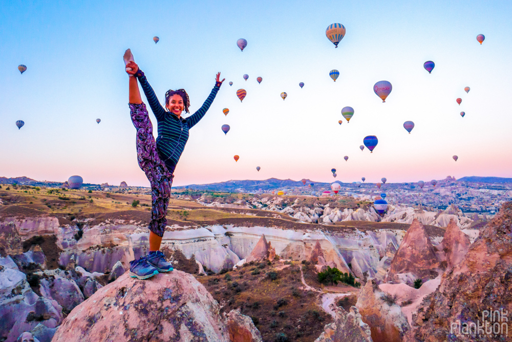 Girl doing yoga pose with t hot air balloons at sunrise in Cappadocia, Turkey