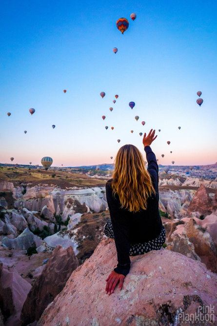 Girl waving at hot air balloons at sunrise in Cappadocia, Turkey