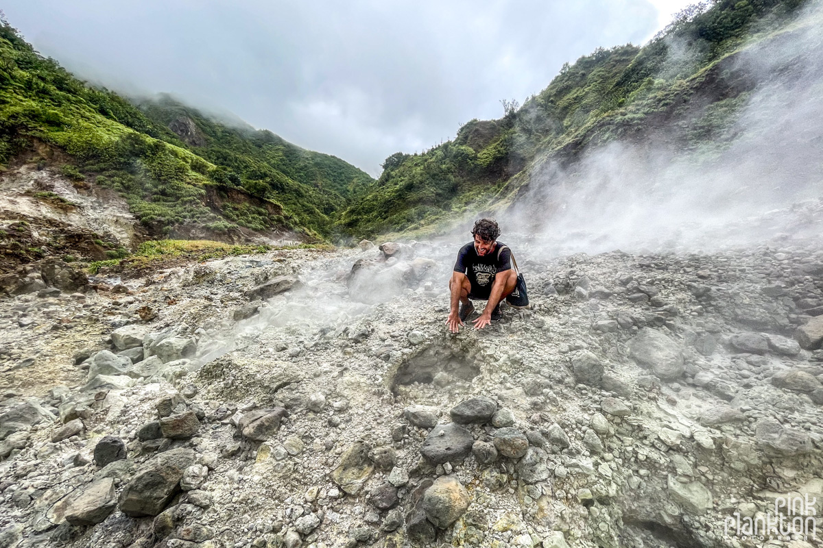Hiker warming his hands in the geothermal steam of the Valley of Desolation along the Boiling Lake Hike in Dominica