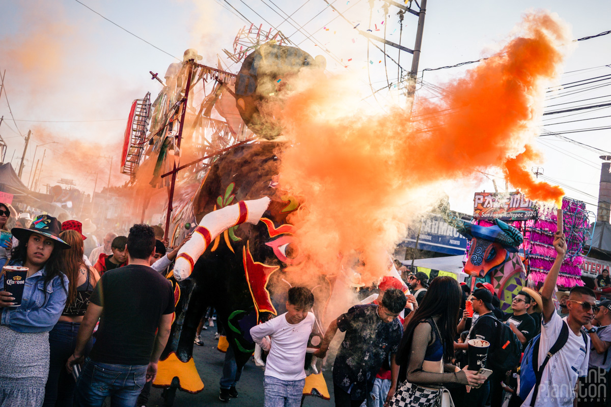 Crowd and bull with orange smoke parading during day at Mexico's Bulls of Fire Festival