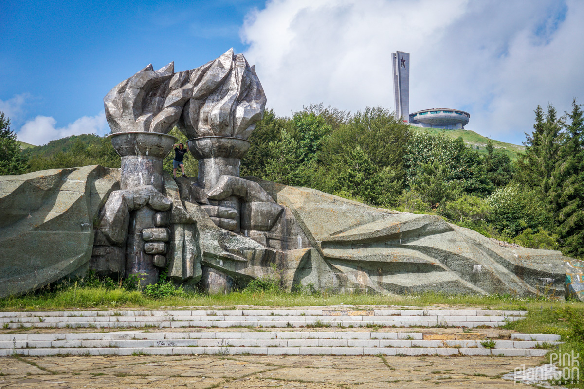 Hands holding flame sculptures with Buzludzha abandoned Communist monument in background