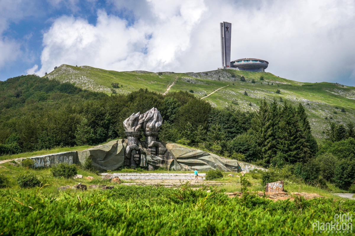 Buzludzha abandoned Communist monument in background with hands holding flame sculptures in front